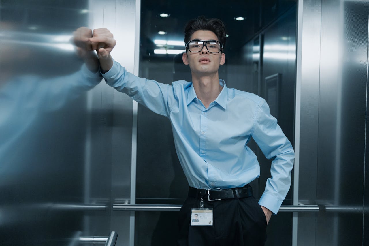 digital Portrait of an Asian man in blue long sleeves with eyeglasses, leaning in an elevator.